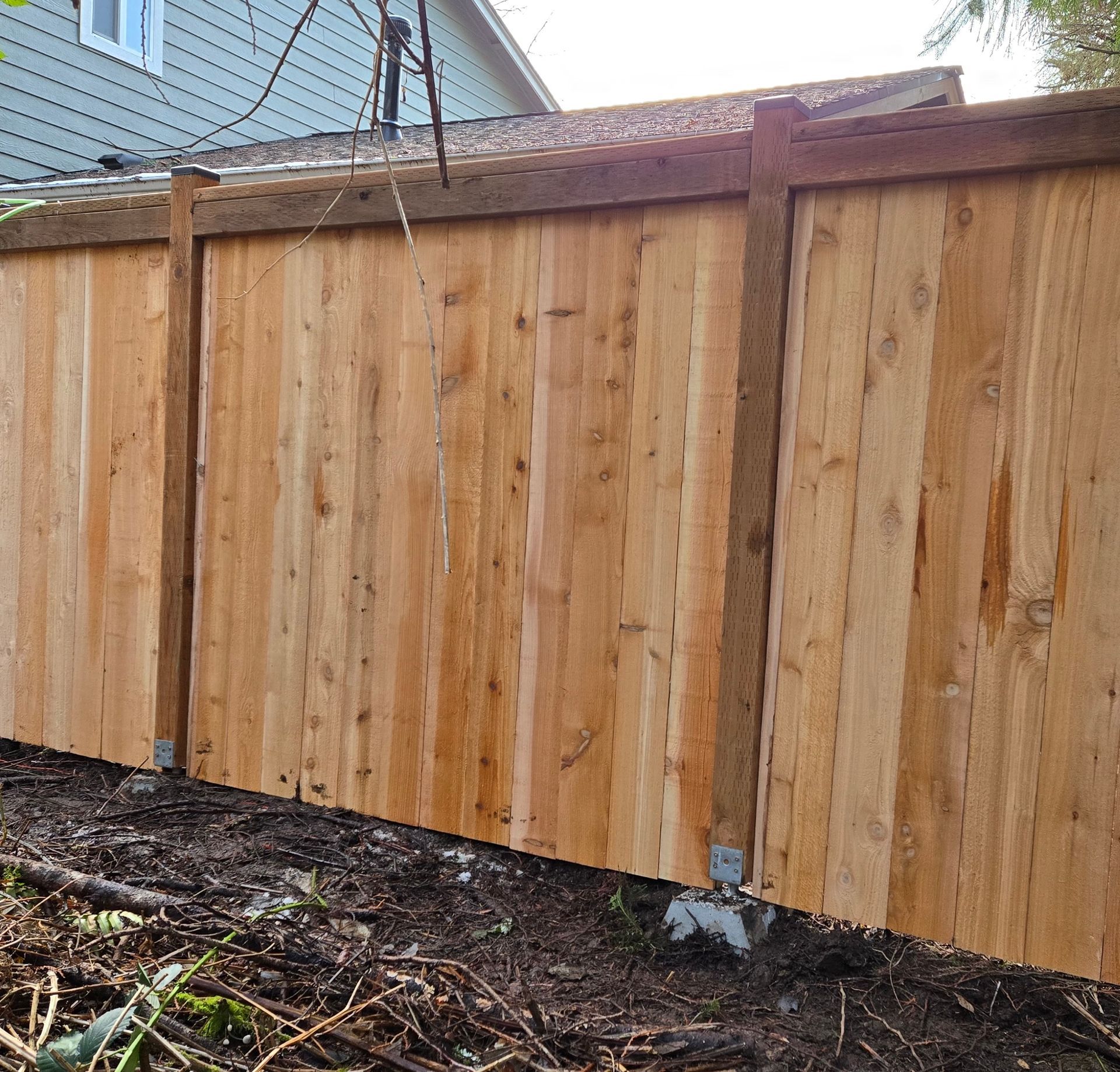 A new cedar wood fence stands outside with panels attached to vertical posts secured in concrete footings at ground level.