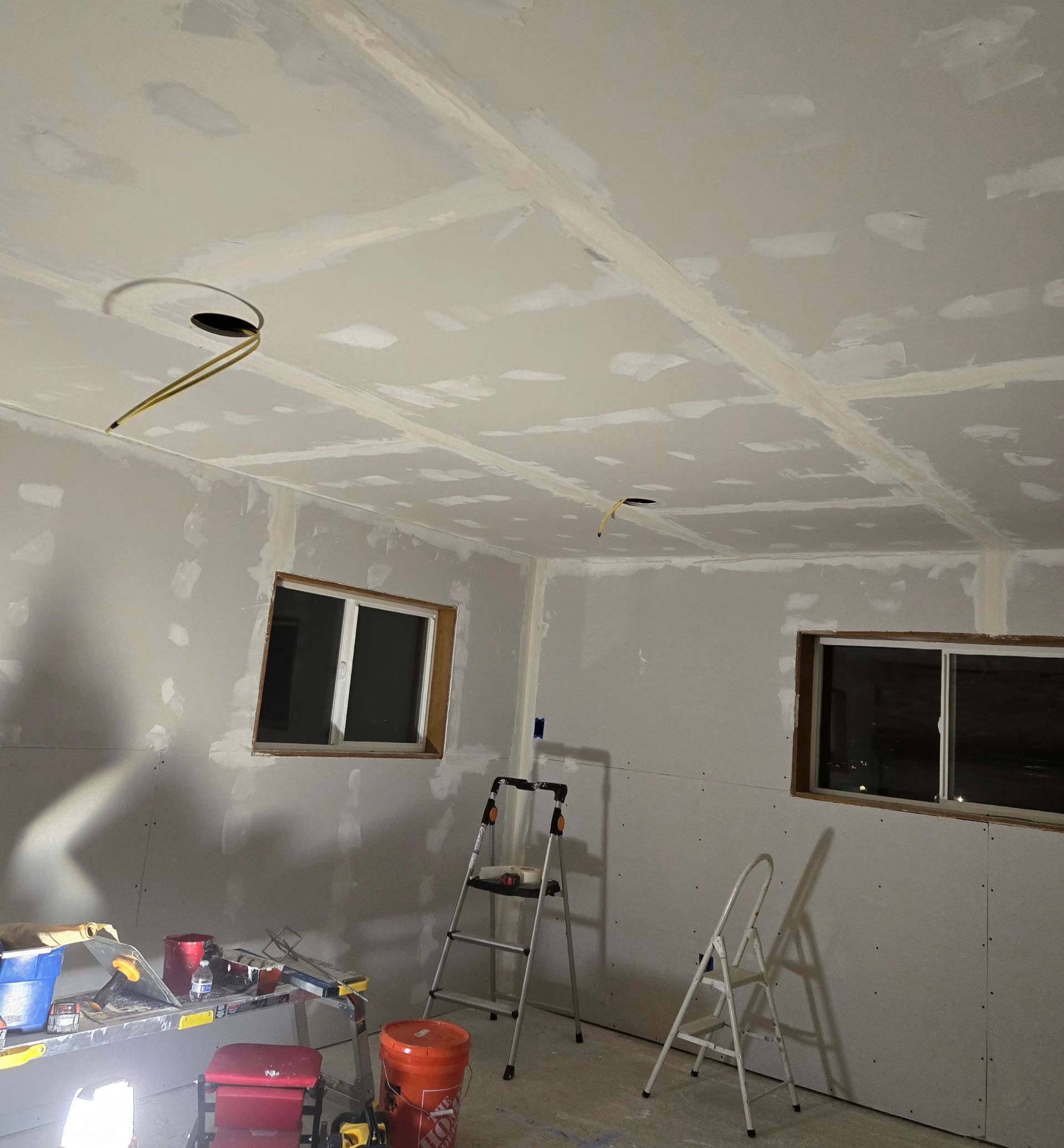 An interior room under construction with drywall installed on walls and ceiling, tape on seams, and two stepladders.