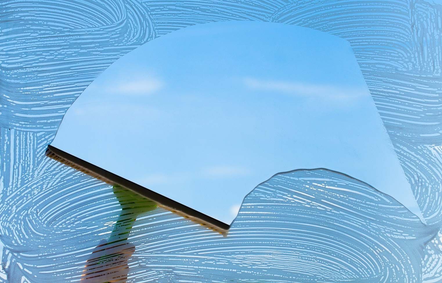 Squeegee cleaning a window, creating a clear area against a soapy, blue background.