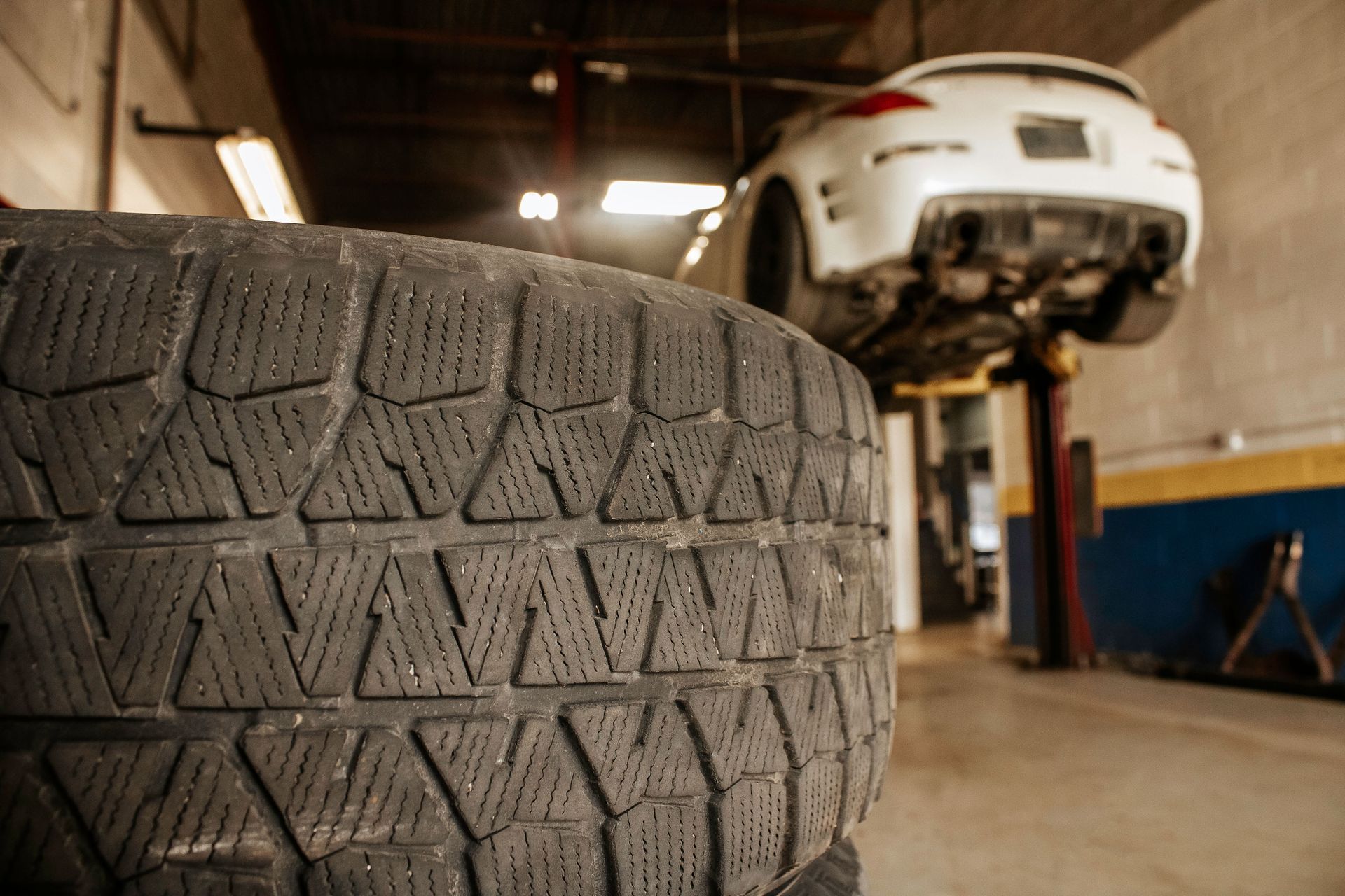Tire in focus, white car on a lift in a garage.