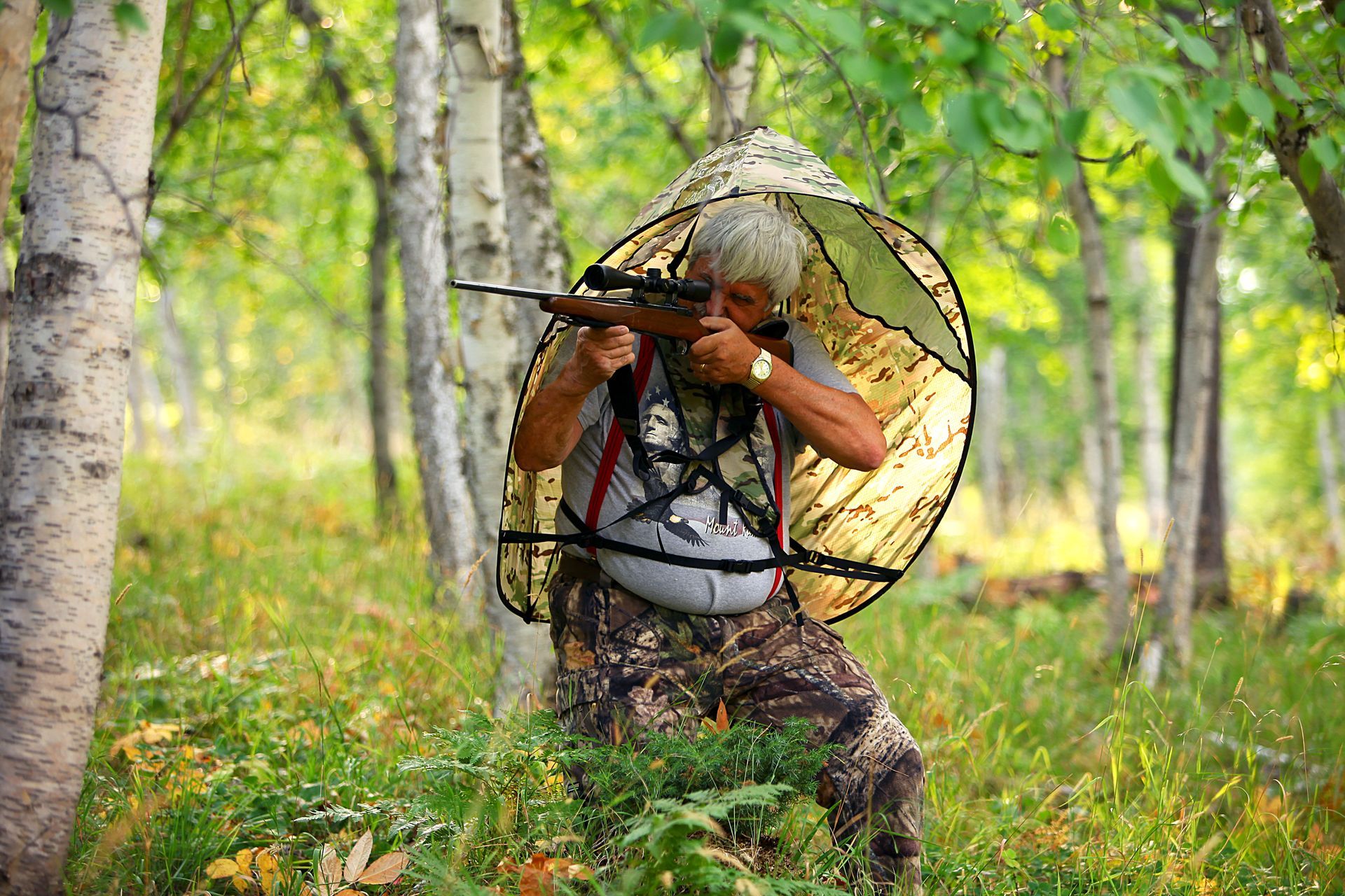 Airsoft player wearing helmet and goggles covered with GOShelter Weathercock Camo Film in with forest overlay, in a wooded area.
