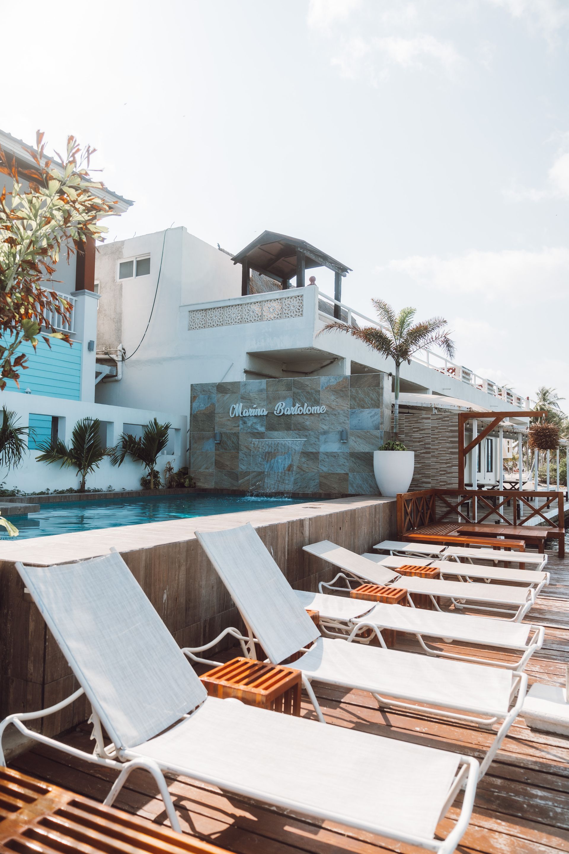 Poolside lounge chairs facing a pool and white building under a sunny sky.