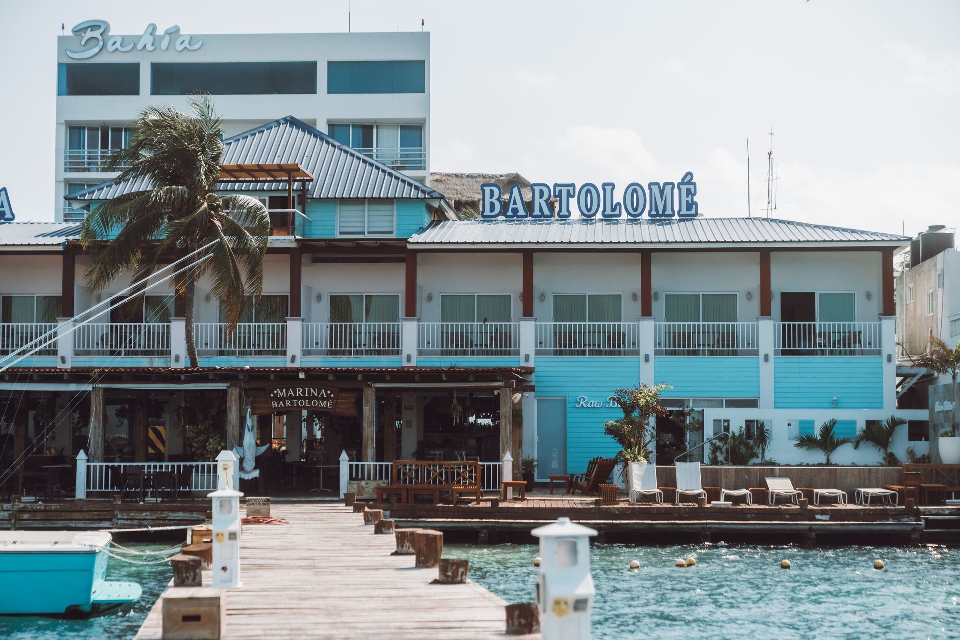 Bartolomé restaurant and hotel exterior, waterfront view. Blue and white building, dock with chairs.