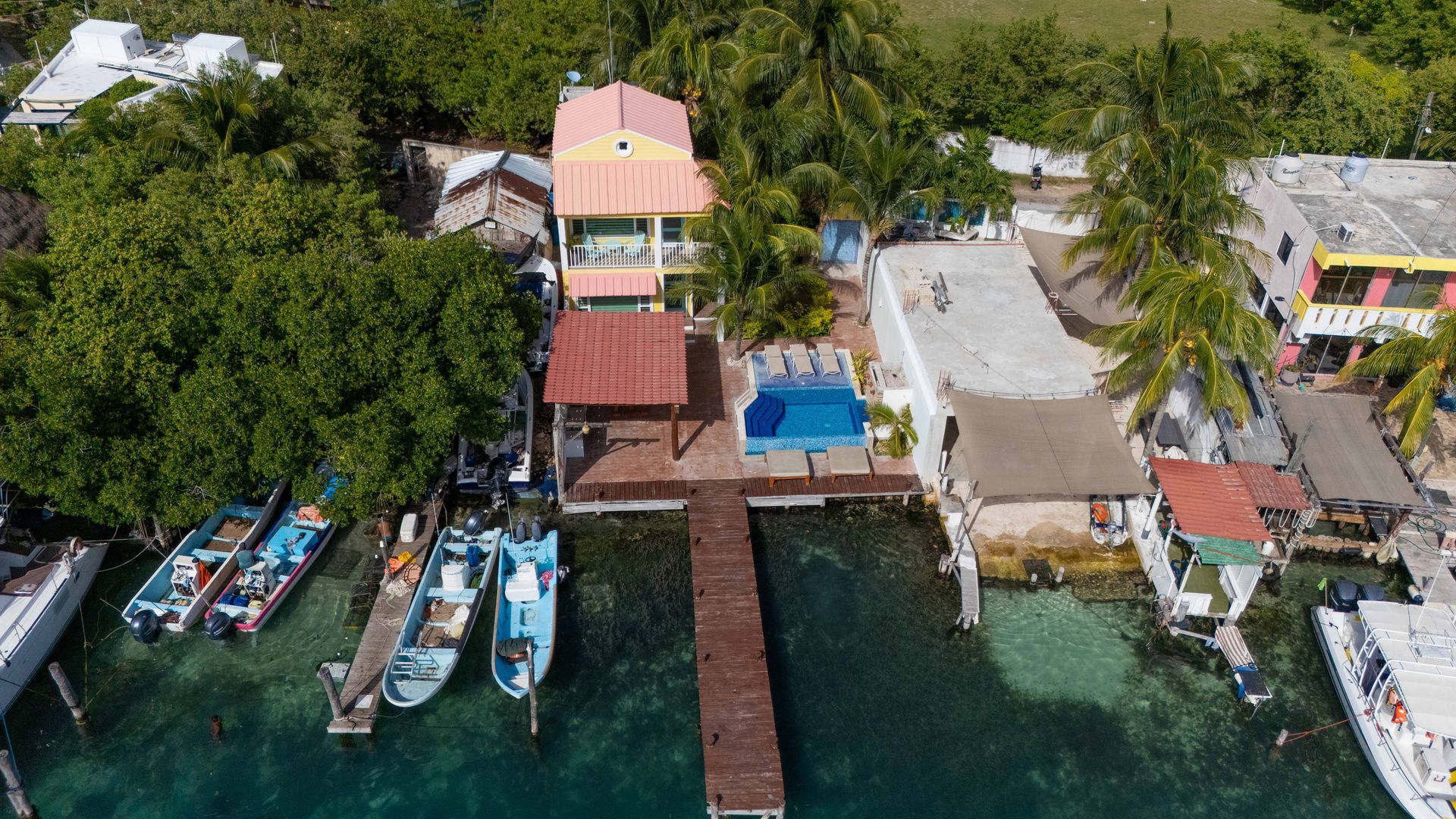 Aerial view of waterfront houses with boats and a dock on turquoise water.