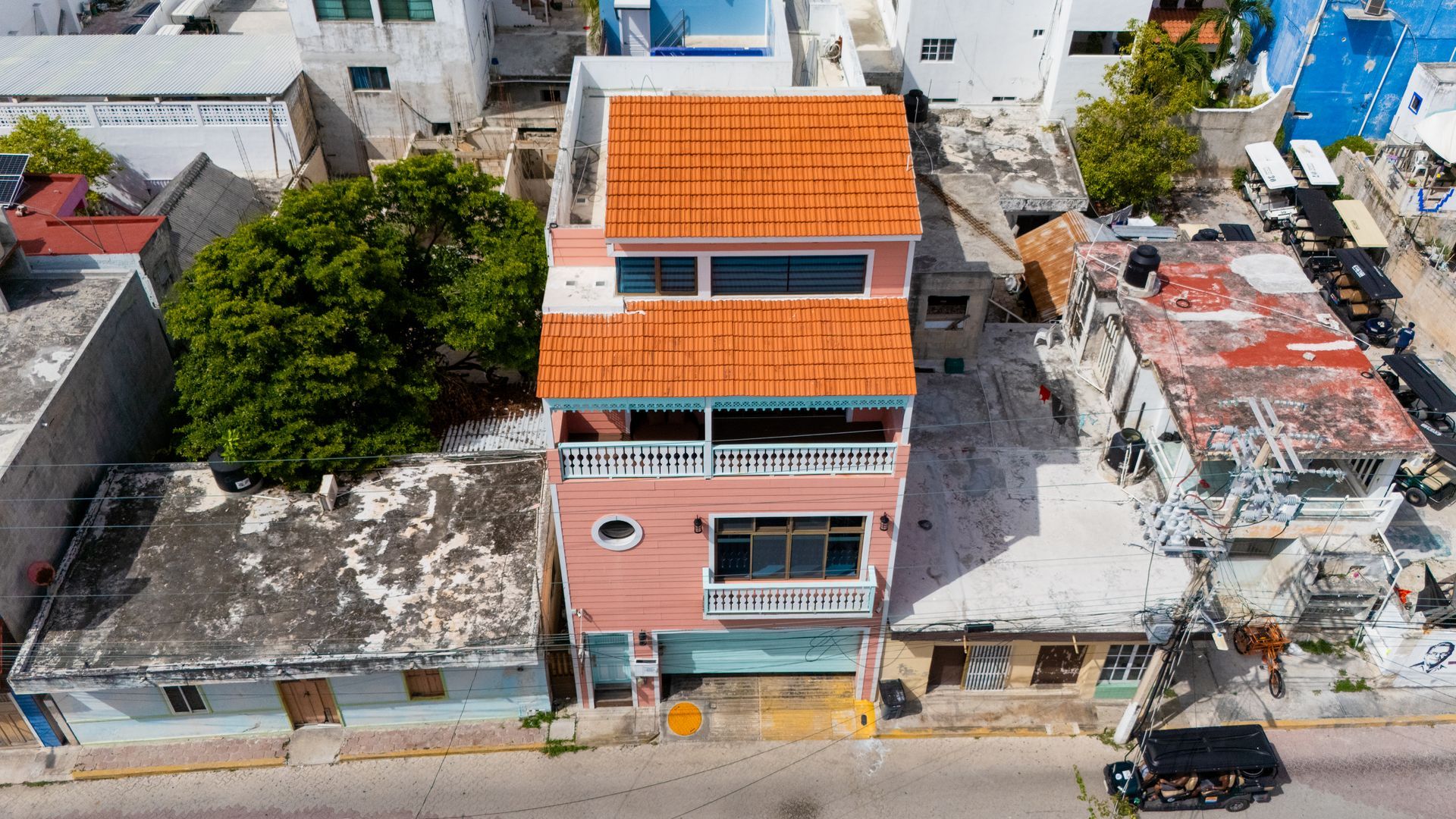 Pink three-story building with orange tiled roof, flanked by smaller buildings, seen from above.