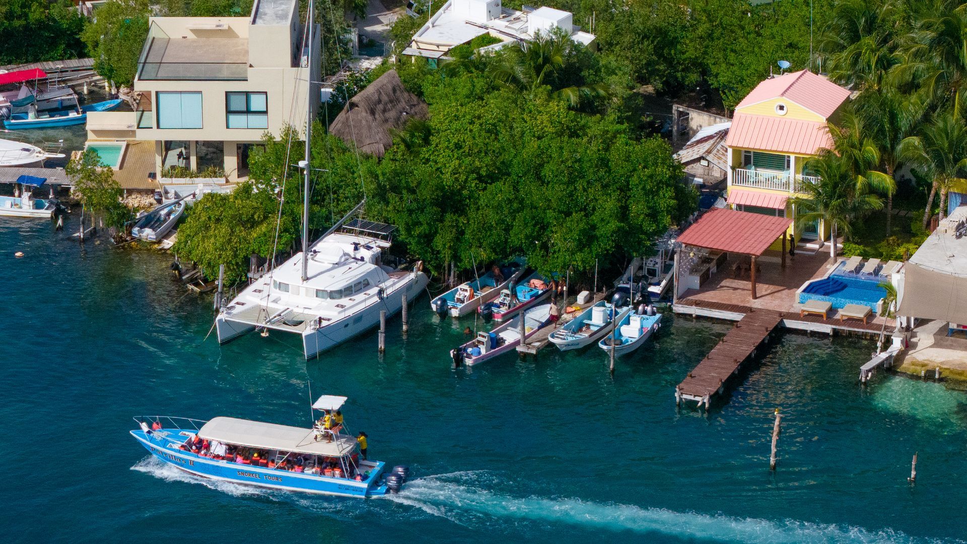 Boats docked by waterfront houses in turquoise water; passenger boat in foreground.