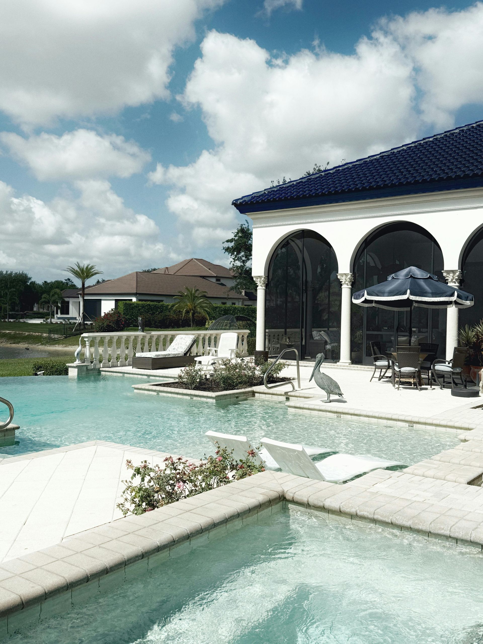 Luxury pool with a house, blue roof, and bright blue sky.