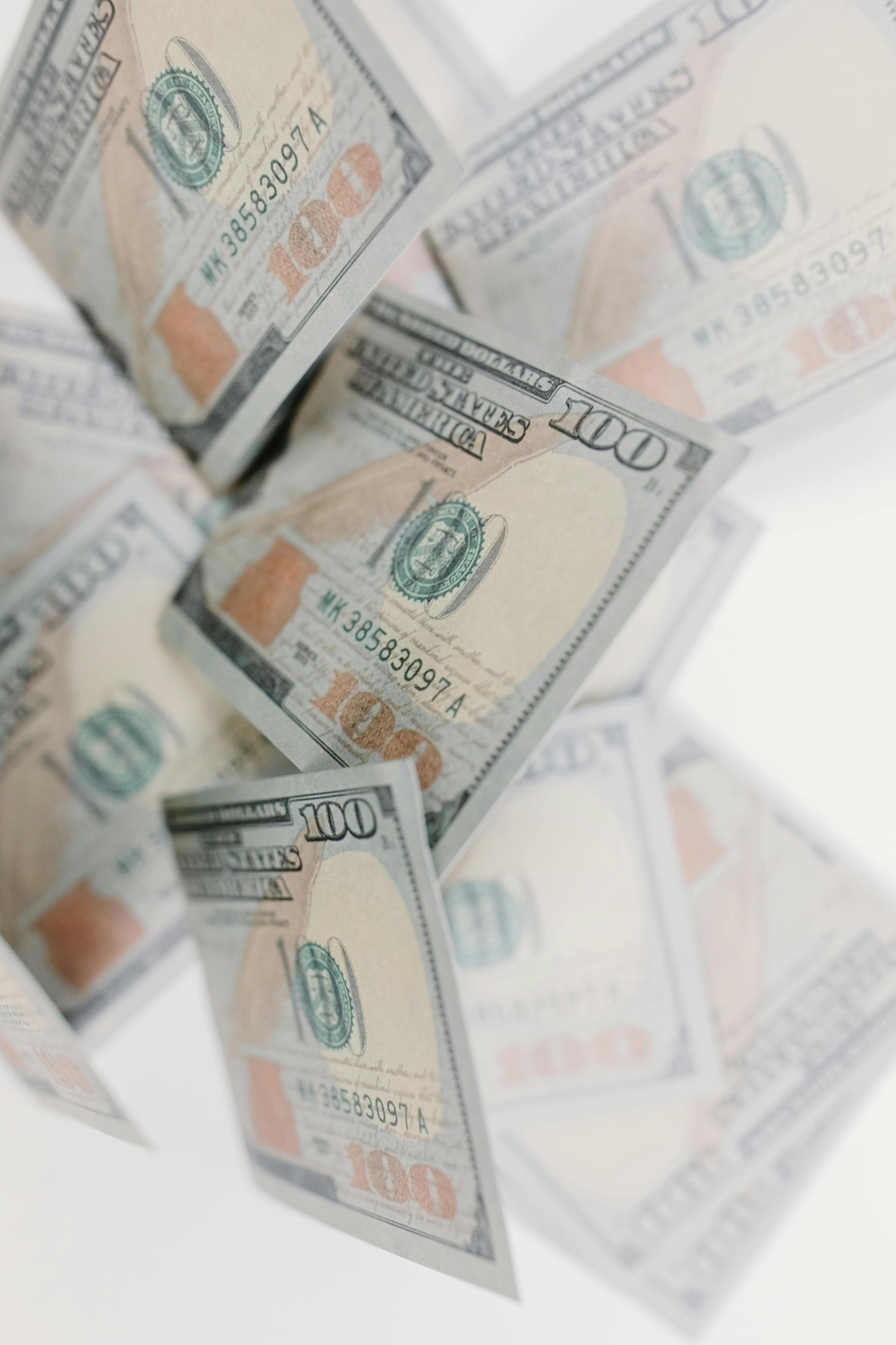 Scattered $100 bills, many in focus, against a blurred white background.