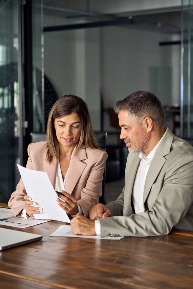 Woman and man reviewing documents at a table in a modern office setting.