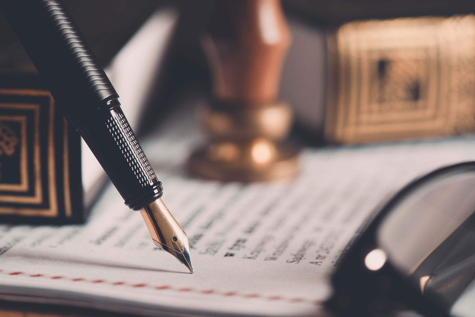 Fountain pen on document; legal theme, with stamp, glasses, and books in soft focus.