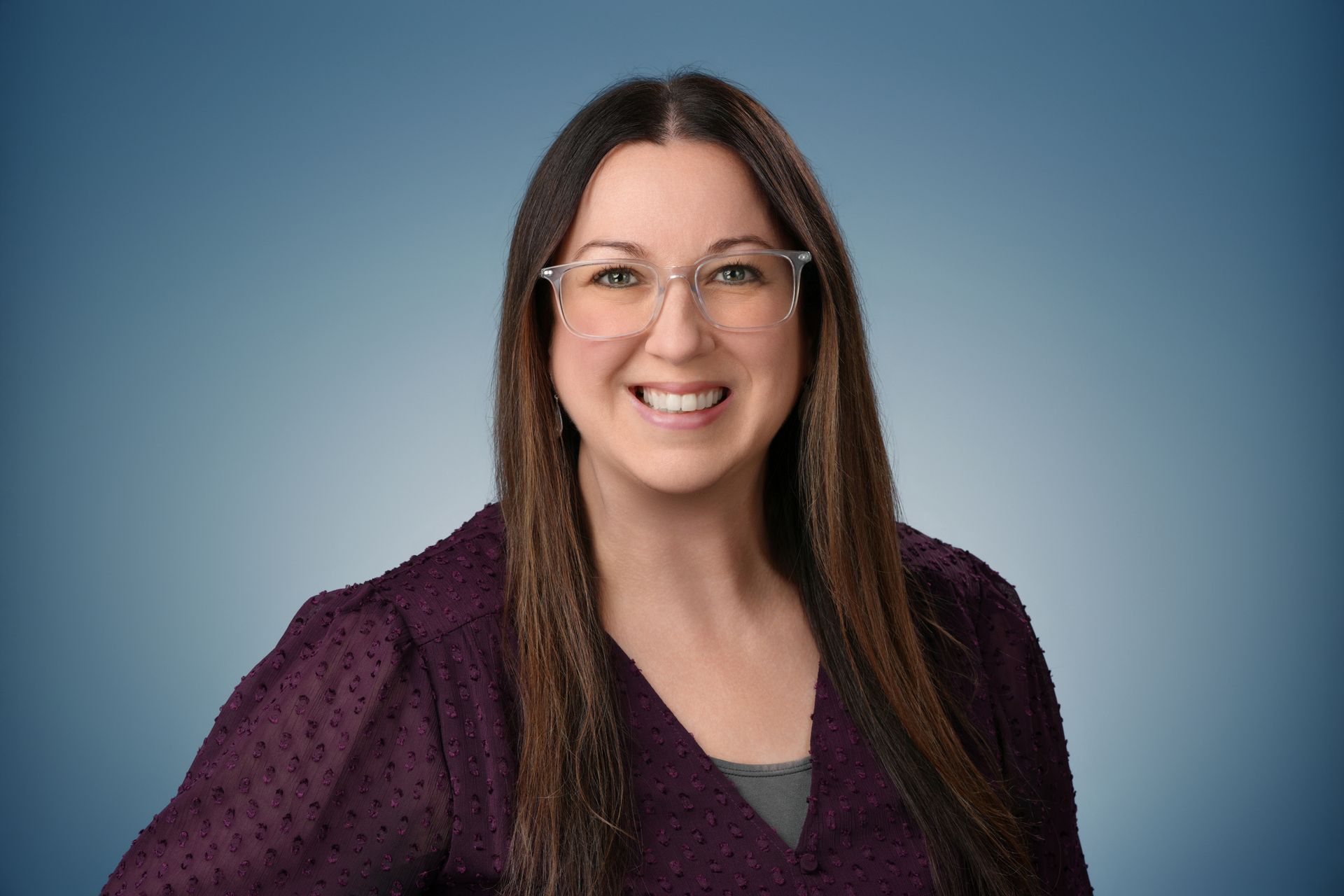 Woman with long brown hair, wearing glasses and yellow top, smiling.