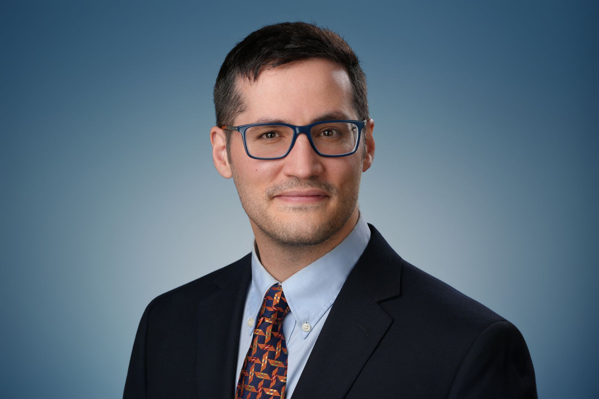 Man in a suit smiling, headshot. White background.