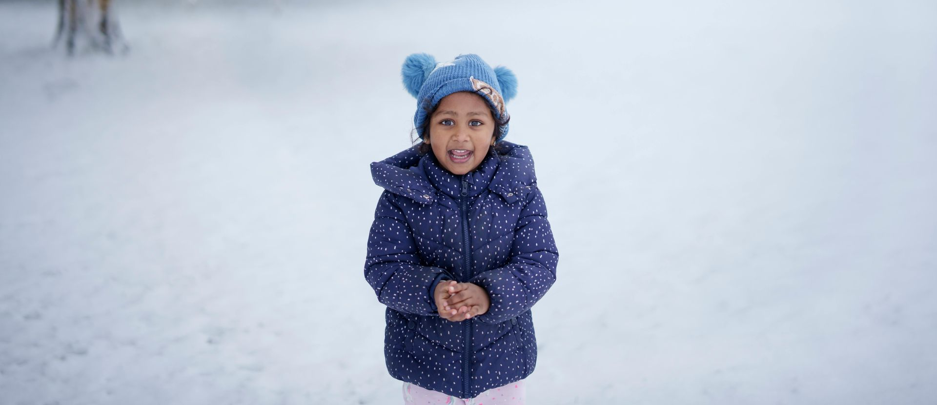 Girl in blue coat and hat in a snowy park, open mouth, looking forward.