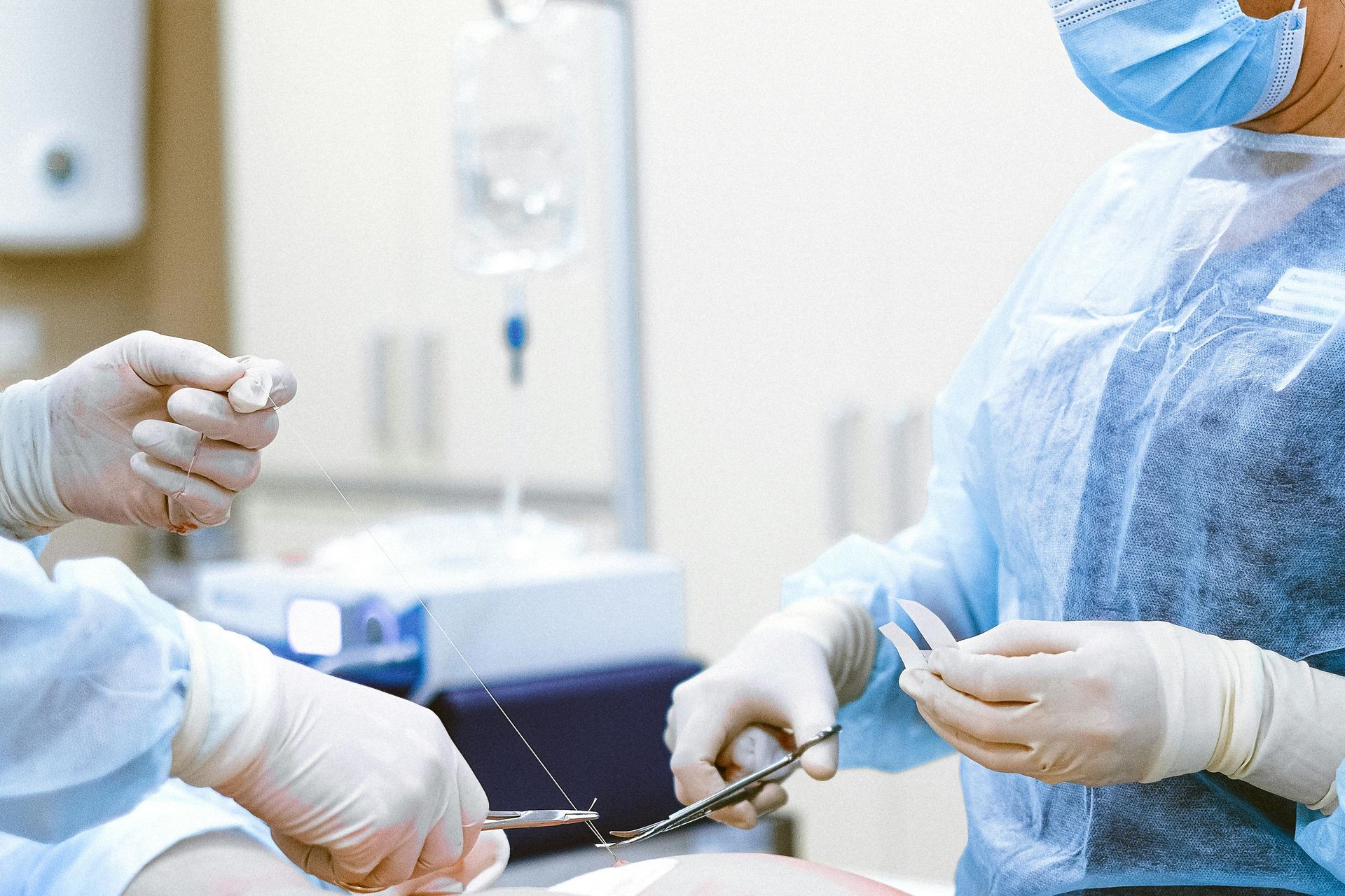 Surgeons in sterile attire, operating room setting; one holds scissors, other holds surgical instrument.