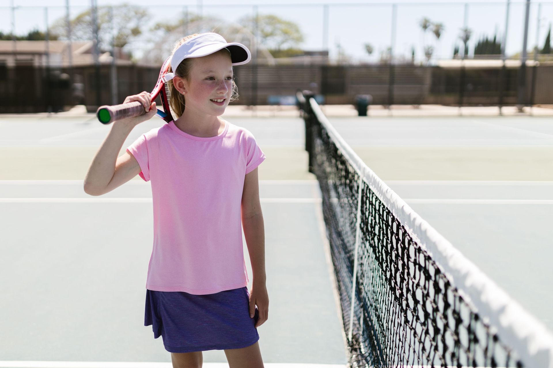 Girl holding a tennis racket on a sunny court beside the net