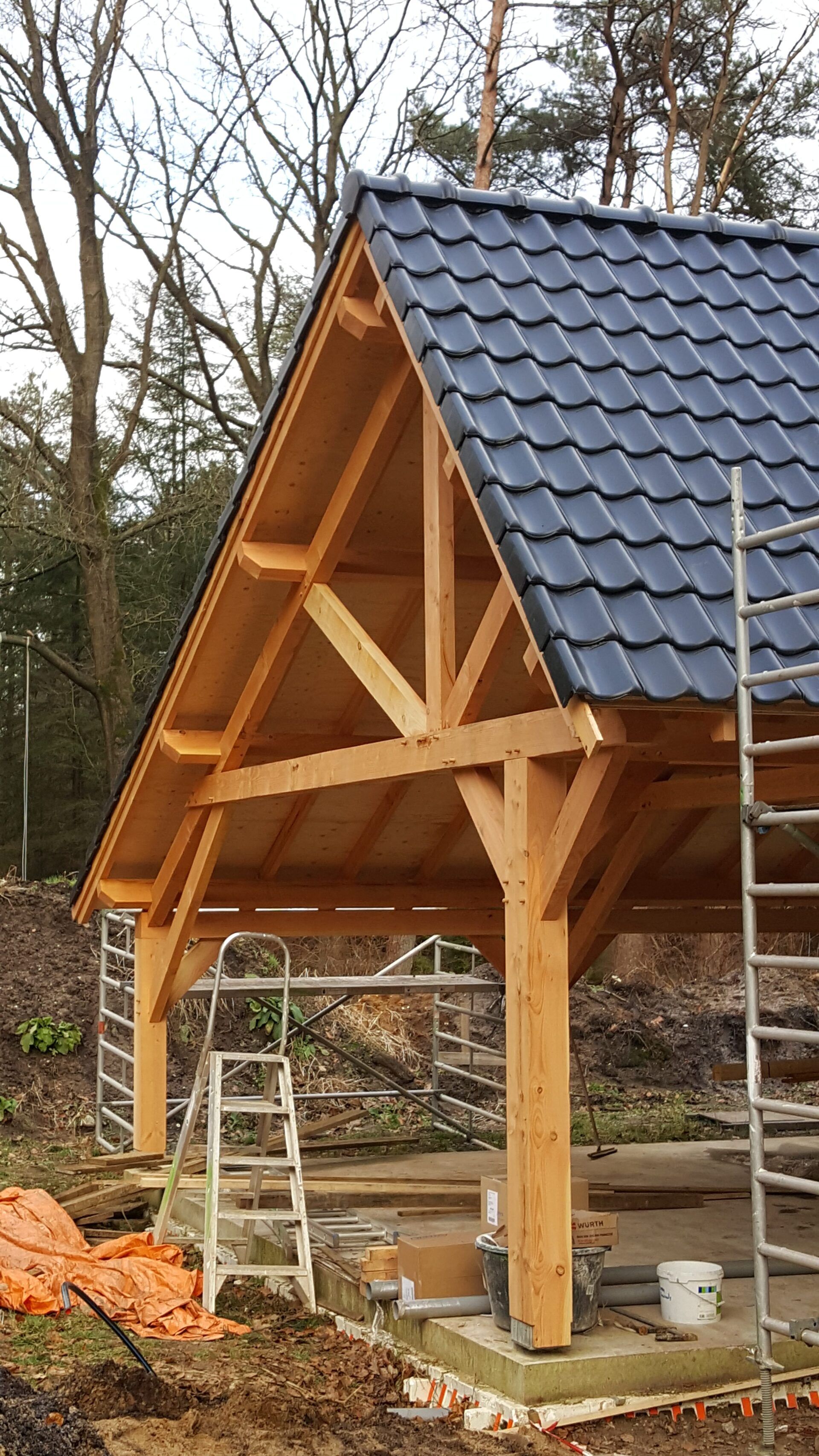 Er wordt een houten constructie met een blauw pannendak gebouwd.