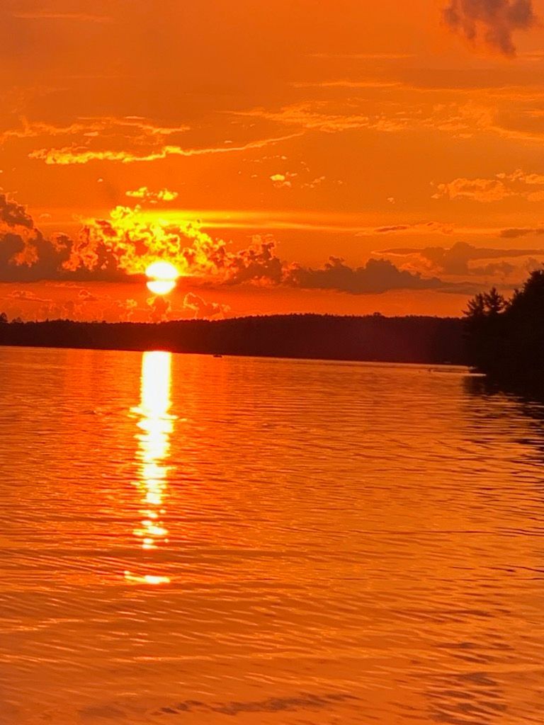 A sunset over a lake with the sun reflected in the water from the view of a lake house