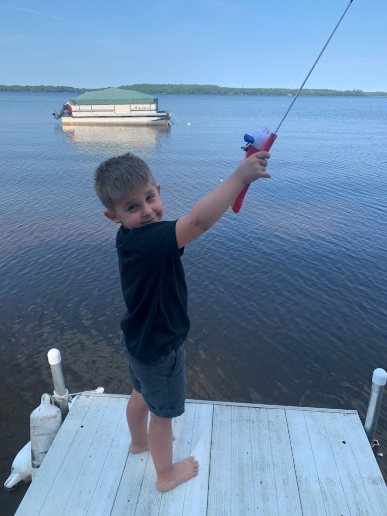 A young boy is standing on a dock holding a fishing rod at his parents lake home