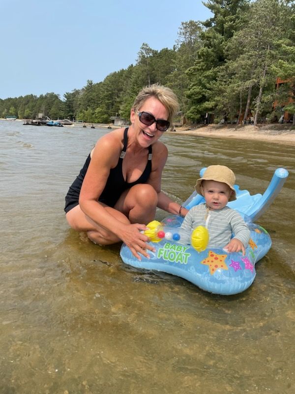 A woman is kneeling next to a baby in an inflatable raft in the water of a lake