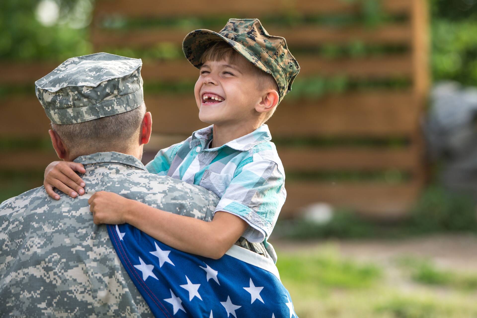 A young boy is hugging a soldier who is holding an american flag.