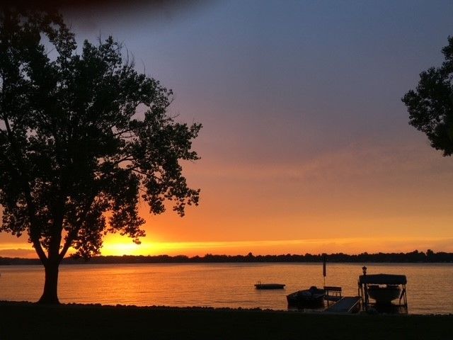 A sunset over a lake from the view of a MN lake house with a tree in the foreground