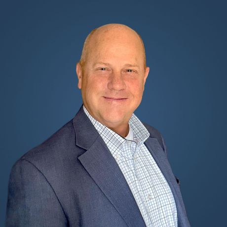 A bald man in a suit and plaid shirt is smiling for the camera.