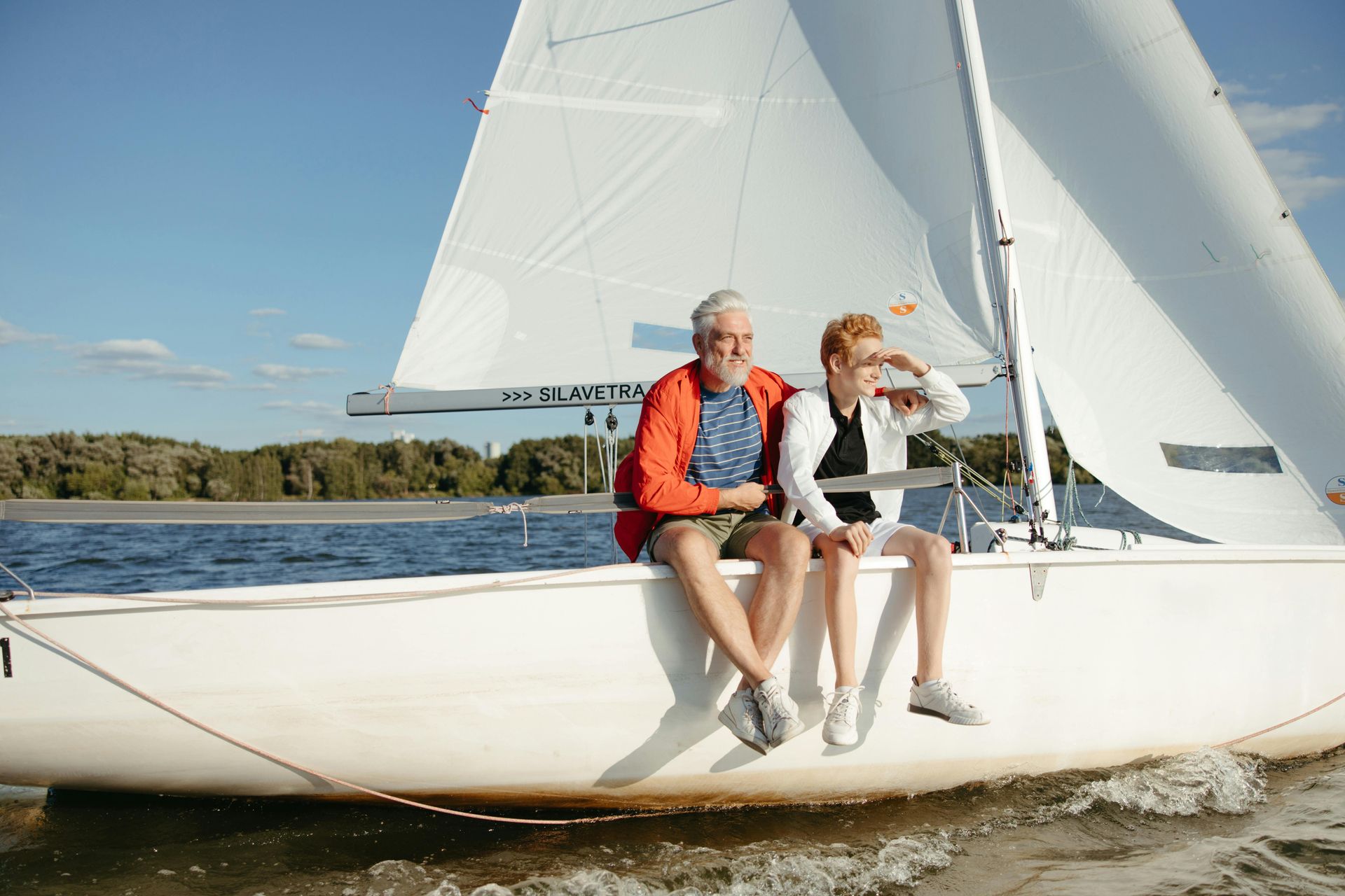 A man and a woman are sitting on the side of a sailboat.