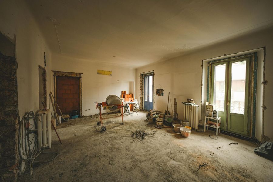 Room under renovation with debris on the floor, walls, and doorway. Contains a cement mixer and radiators.
