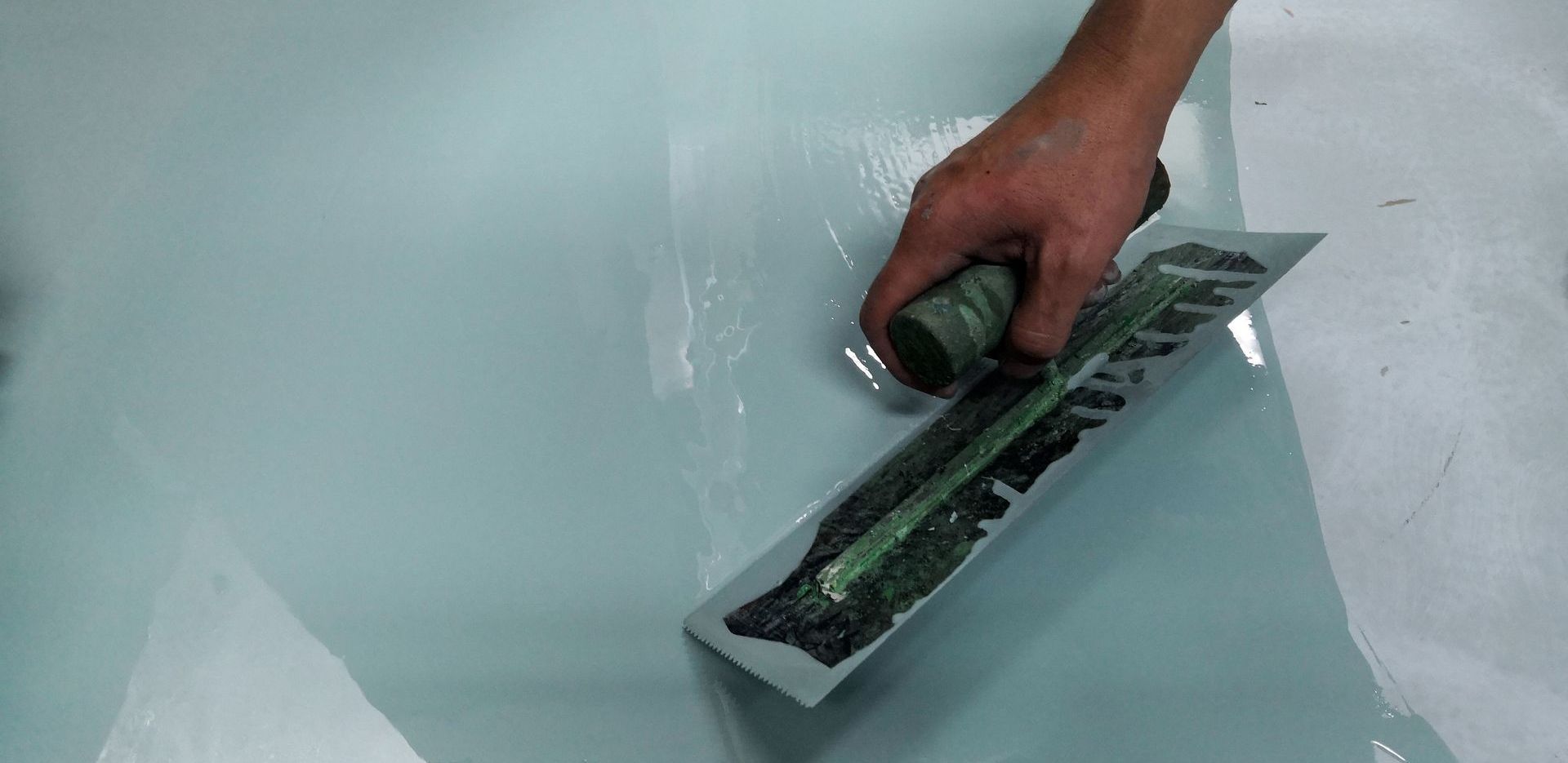 Une personne utilisant une truelle pour étaler un revêtement époxy bleu clair sur un sol.