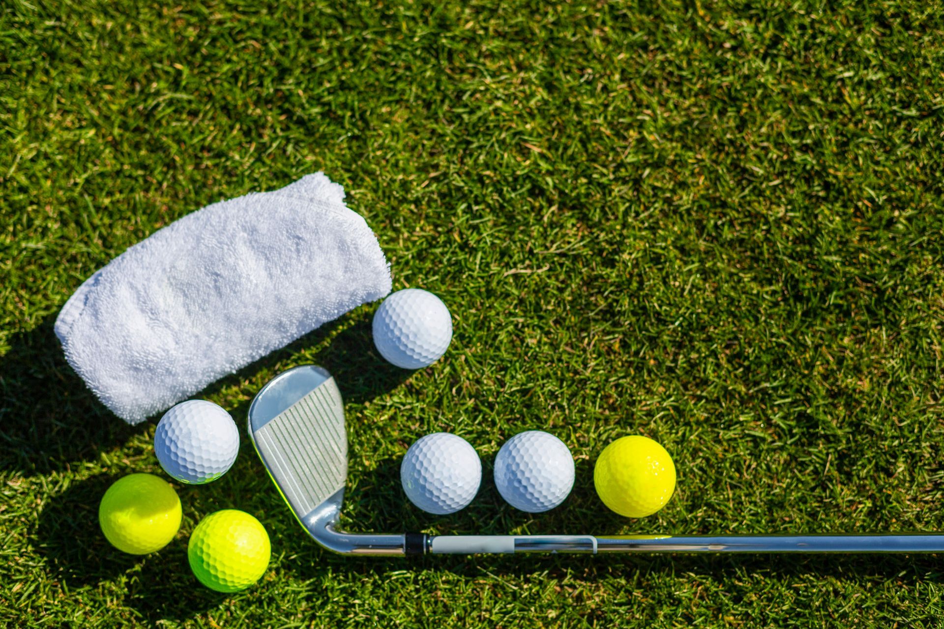 Un club de golf, des balles de golf et une serviette sont sur l'herbe.