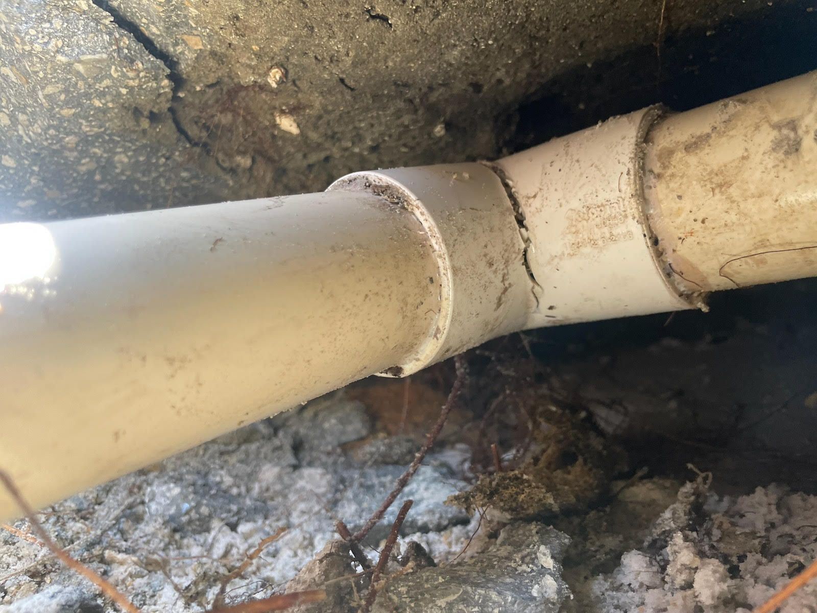 Close-up of two white PVC pipes joined by a damaged coupler in a dirty floor area