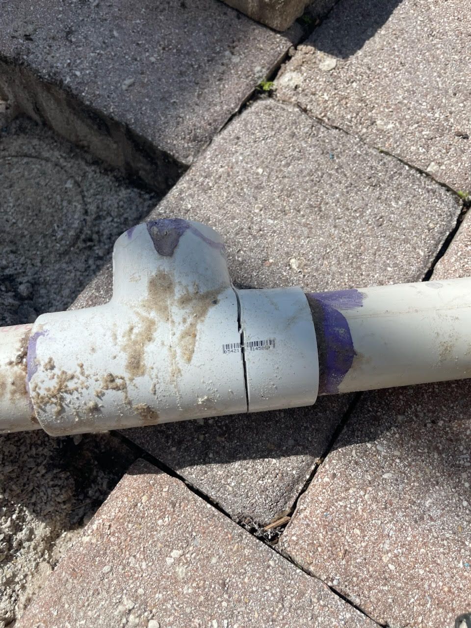 Broken white PVC pipe joint on a stone patio, with dirt stains and a purple repair band