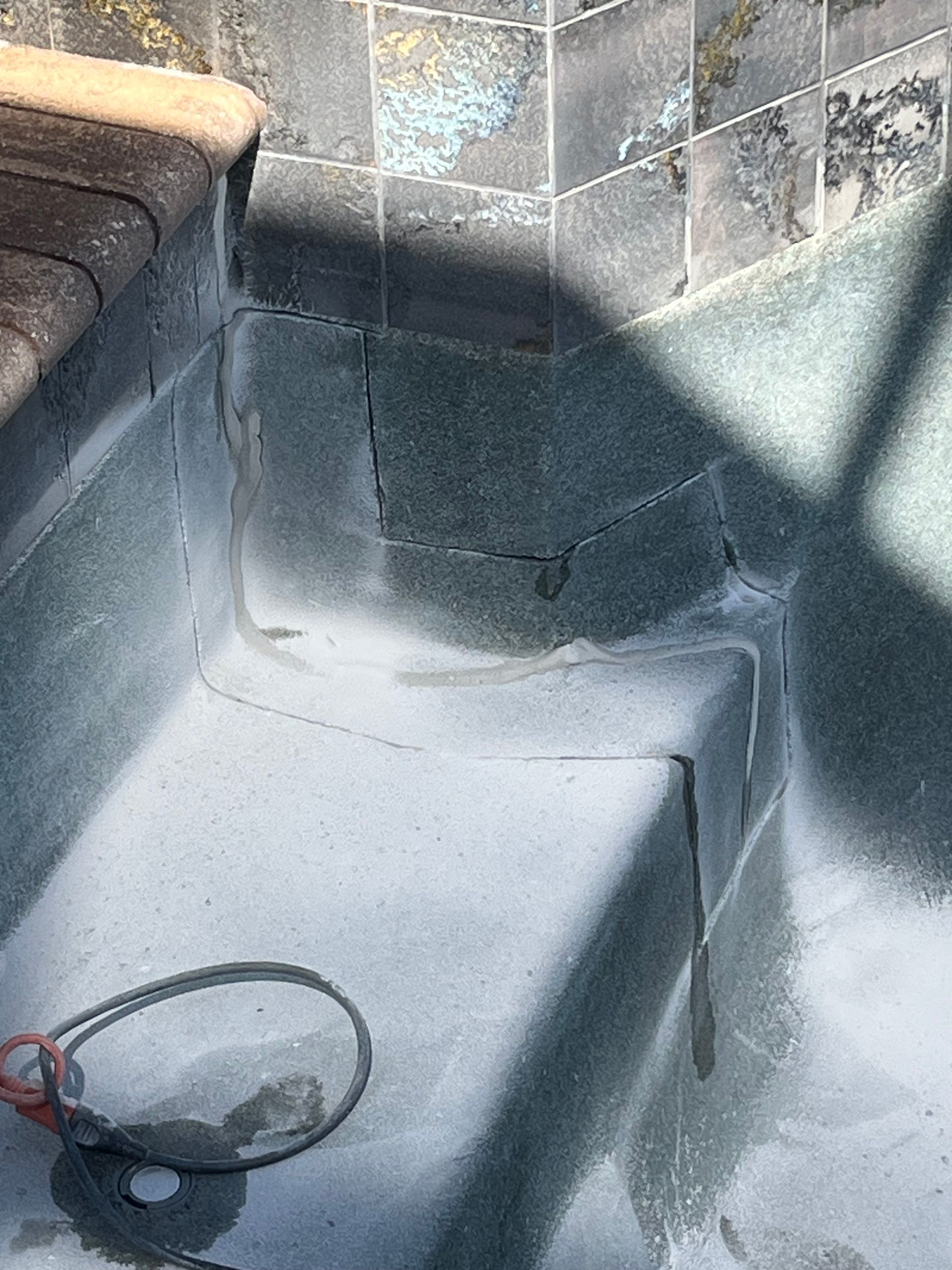 Damaged gray tiled corner with cracked wall and floor, lit by strong sunlight