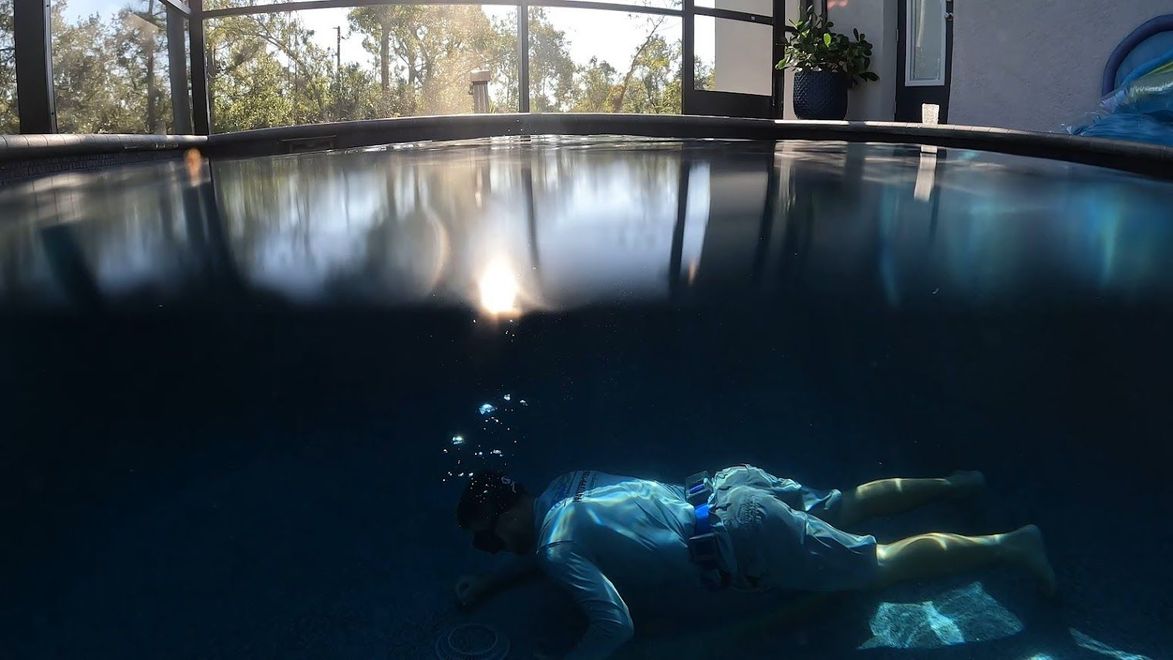 Person snorkeling in a dark blue indoor pool with bright sunlight reflecting on the water