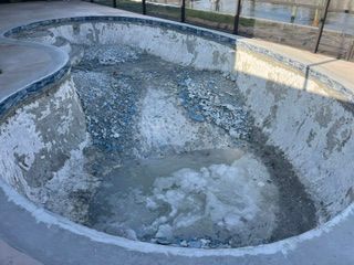 Empty, cracked concrete pool basin with peeling blue paint and a cloudy puddle at the bottom