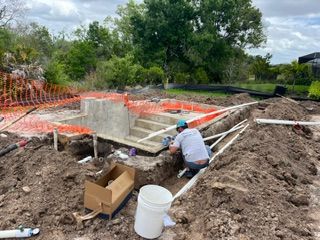 Worker at a construction site inspecting a concrete foundation trench with orange safety fencing.