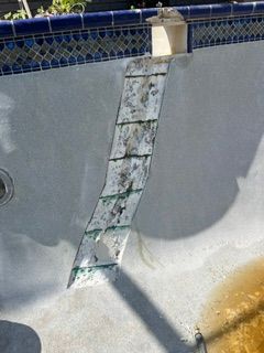 Damaged pool wall with peeling white panel and green stains near blue tile trim