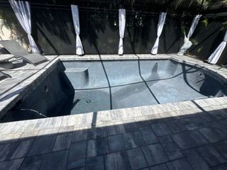 Rectangular in-ground pool with black cover, surrounded by stone decking and white patio curtains