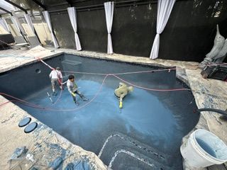 Three people cleaning an empty indoor swimming pool with hoses and water spray