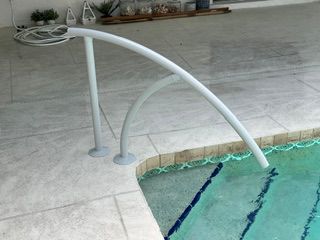 Curved silver handrail descending into a shallow outdoor pool beside a tiled deck