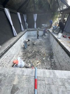Workers cleaning a drained indoor pool with dark walls and white curtains on the sides