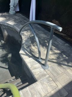Curved metal handrail beside a pool edge on a tiled walkway with sunlight and shadows