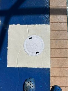Blue floor with a white square panel and circular drain cover, beside a tan tiled edge.