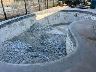 Empty concrete pool under renovation with rubble and a drain visible inside