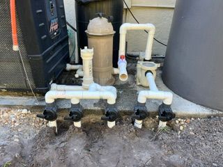 Outdoor PVC plumbing pipes and valves beside utility tanks over muddy ground