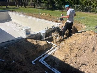 Worker installing white PVC pipes beside a concrete pool under construction
