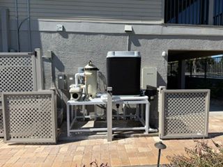 Outdoor water filtration equipment on a patio beside a building, with metal panels and a black tank.