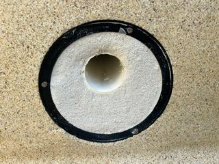 Black-rimmed circular wall opening with a white interior on a speckled beige surface