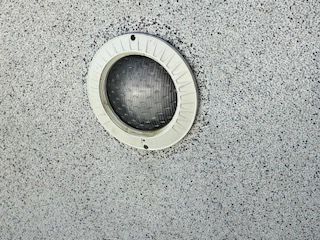 Circular recessed light fixture on a speckled gray ceiling panel.