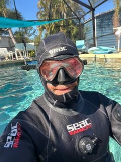 Person in a black Seac wetsuit and mask smiling in a pool under a shaded canopy